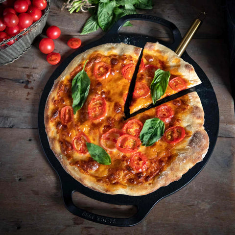 Plancha para pizza Victoria con pizza de jitomate y albahaca, una rebanada separada