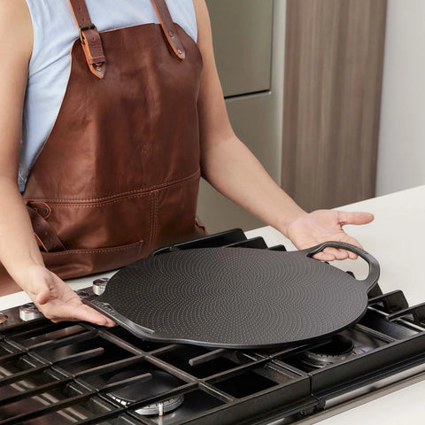 Persona sosteniendo plancha para pizza Victoria con superficie circular texturizada y dos asas