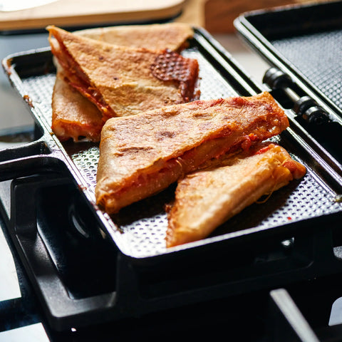 Sanduchera Victoria abierta con sándwiches triangulares tostados sobre la estufa