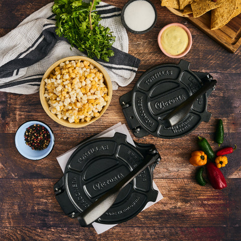 Dos tortilladoras Victoria de distintos tamaños rodeadas de maíz, chiles y totopos