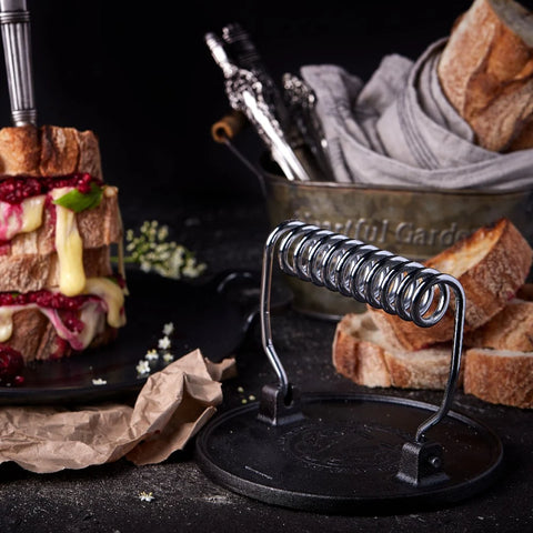 Prensa para hamburguesa Victoria con mango de espiral junto a sándwiches de queso